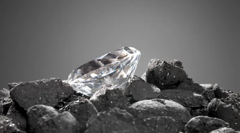 Ein geschliffener Diamant liegt auf dunkler Kohle.