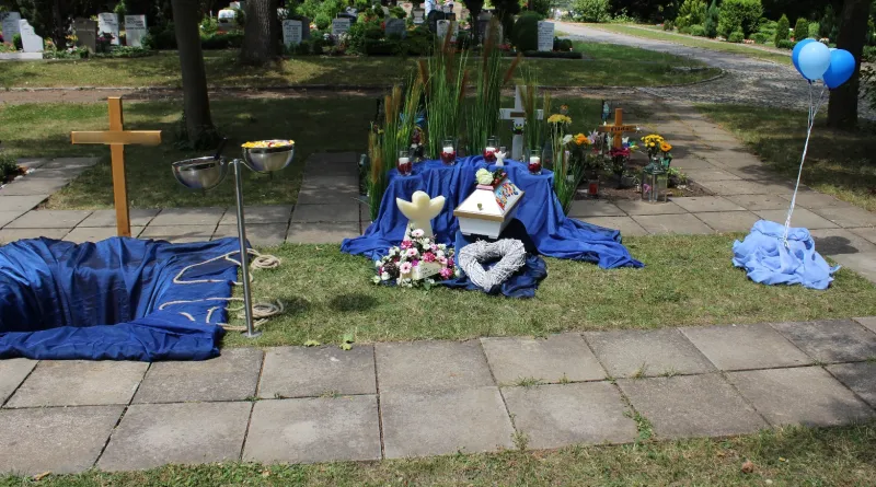 Eine individuell gestaltete Trauerfeier auf einem Friedhof mit Kreuz.